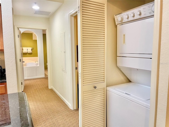 laundry room featuring light carpet and stacked washer and dryer