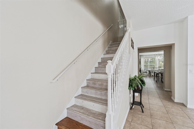 stairs featuring a notable chandelier, a textured ceiling, and tile patterned flooring