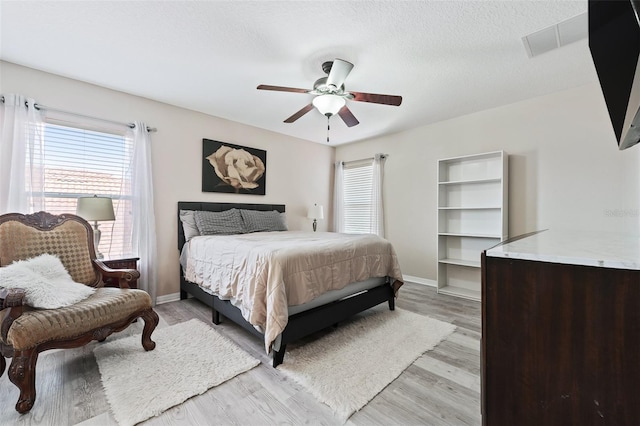 bedroom with a textured ceiling, light hardwood / wood-style flooring, and ceiling fan