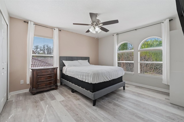 bedroom with a closet, ceiling fan, light hardwood / wood-style floors, and multiple windows