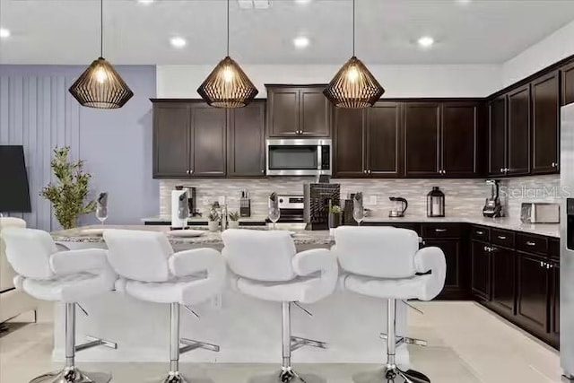 kitchen featuring a center island with sink, a breakfast bar area, decorative backsplash, and decorative light fixtures