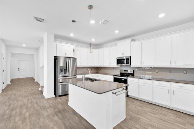 kitchen featuring appliances with stainless steel finishes, decorative light fixtures, white cabinetry, sink, and a kitchen island with sink