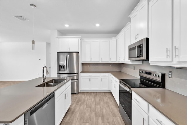 kitchen with appliances with stainless steel finishes, sink, pendant lighting, and white cabinets