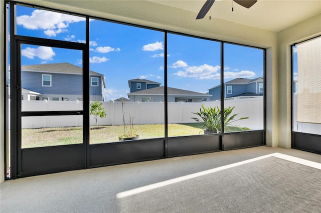 unfurnished sunroom featuring a residential view and ceiling fan