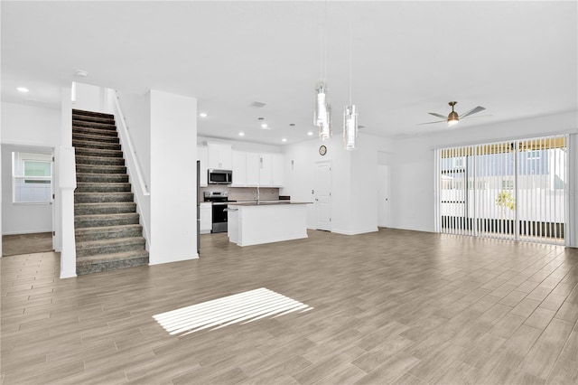 unfurnished living room with light wood finished floors, ceiling fan, stairway, and recessed lighting