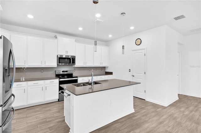 kitchen featuring a center island with sink, stainless steel appliances, dark countertops, light wood-style flooring, and a sink