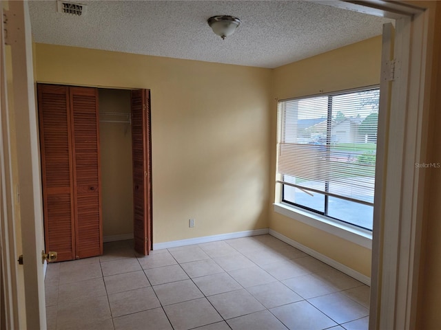 unfurnished bedroom featuring a closet, a textured ceiling, and light tile patterned flooring