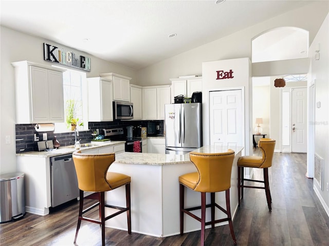 kitchen featuring stainless steel appliances, white cabinetry, vaulted ceiling, and decorative backsplash