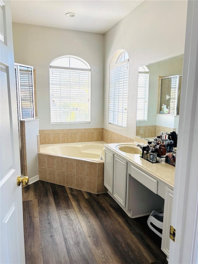 bathroom featuring a relaxing tiled tub, vanity, wood-type flooring, and a healthy amount of sunlight