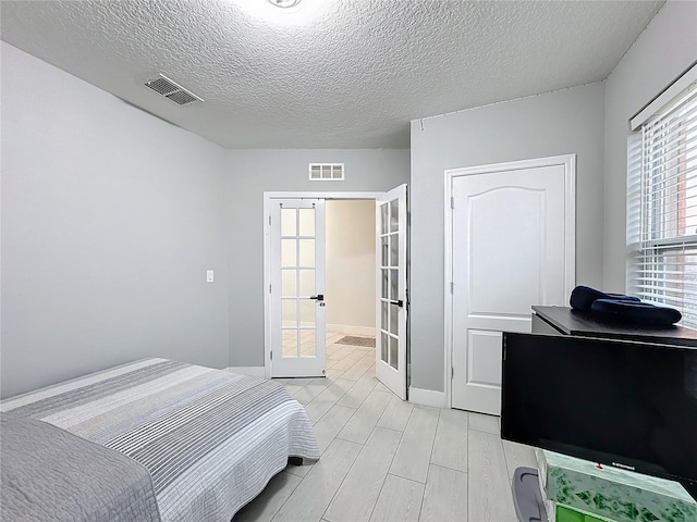 bedroom with light hardwood / wood-style flooring, a textured ceiling, and french doors