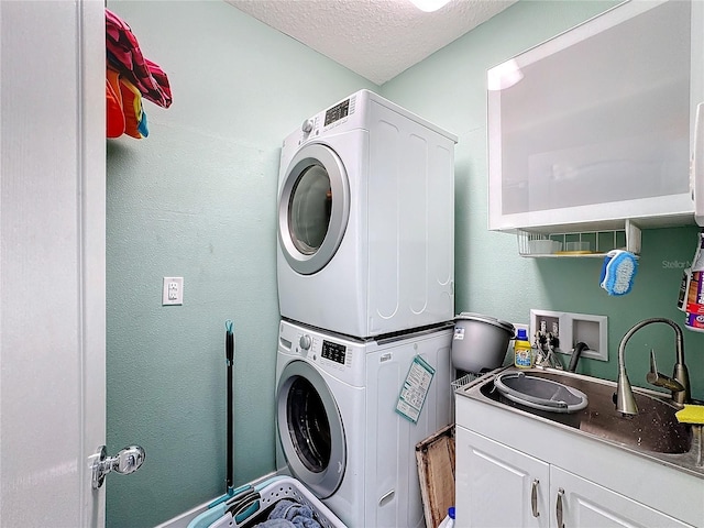 laundry room with cabinets, stacked washing maching and dryer, sink, and a textured ceiling