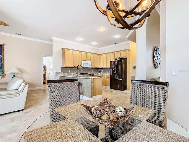 kitchen with light brown cabinets, a kitchen breakfast bar, backsplash, black fridge, and ornamental molding