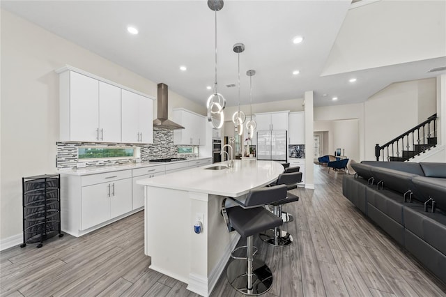 kitchen with gas stovetop, white cabinets, decorative light fixtures, an island with sink, and wall chimney exhaust hood