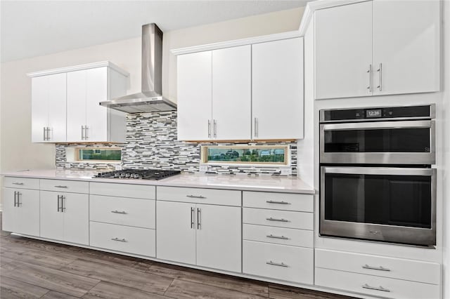 kitchen featuring backsplash, white cabinetry, wall chimney exhaust hood, and appliances with stainless steel finishes