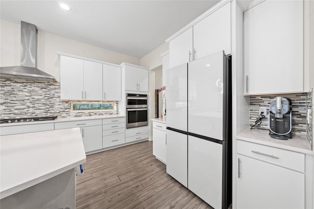 kitchen featuring white refrigerator, white cabinets, gas stovetop, and wall chimney range hood