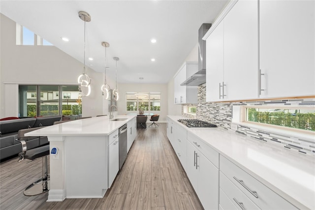 kitchen featuring white cabinetry, wall chimney range hood, stainless steel appliances, sink, and hanging light fixtures