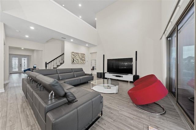 living room featuring light wood-type flooring, a towering ceiling, and french doors