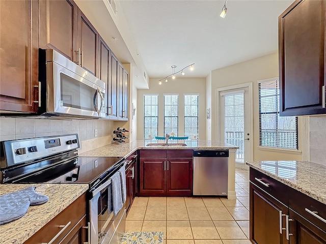 kitchen featuring sink, light tile patterned floors, appliances with stainless steel finishes, kitchen peninsula, and backsplash