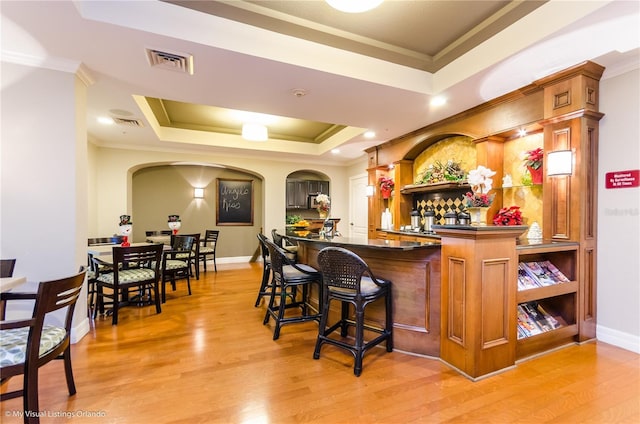 bar with crown molding, a tray ceiling, and light wood-type flooring