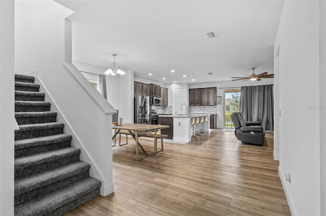 living room with ceiling fan with notable chandelier, sink, and light hardwood / wood-style flooring