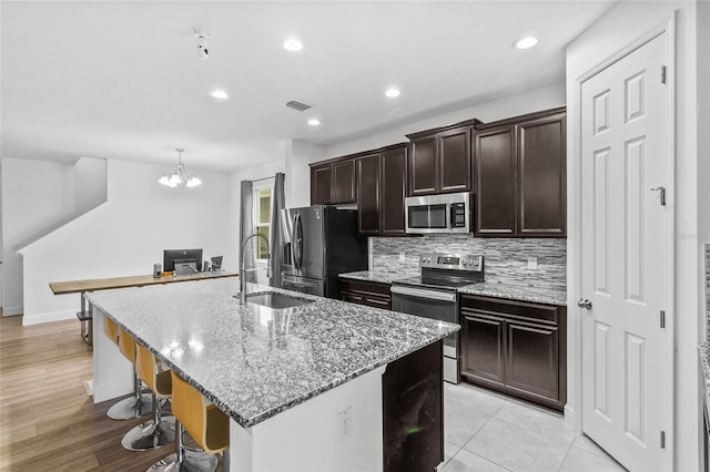 kitchen with a breakfast bar, sink, backsplash, stainless steel appliances, and a center island with sink