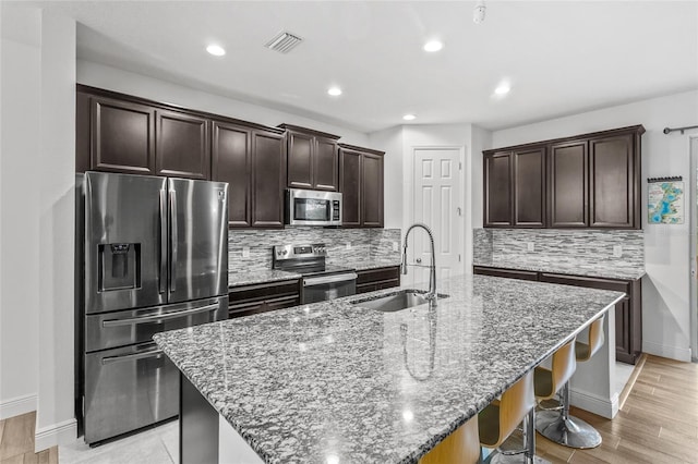 kitchen with a kitchen bar, sink, a center island with sink, dark stone countertops, and appliances with stainless steel finishes