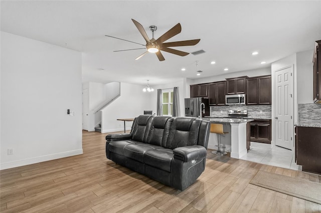 living room featuring ceiling fan with notable chandelier and light hardwood / wood-style flooring