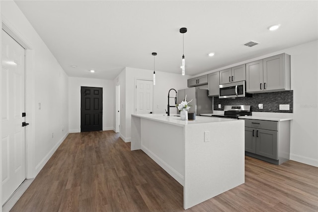 kitchen with decorative light fixtures, an island with sink, gray cabinetry, backsplash, and stainless steel appliances