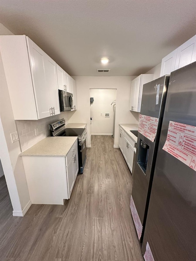 kitchen featuring tasteful backsplash, stainless steel appliances, hardwood / wood-style floors, and white cabinets