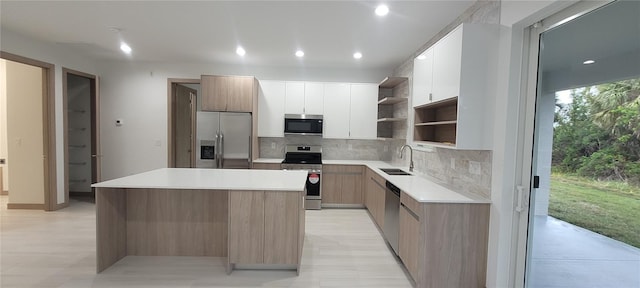 kitchen featuring appliances with stainless steel finishes, sink, white cabinets, backsplash, and a center island