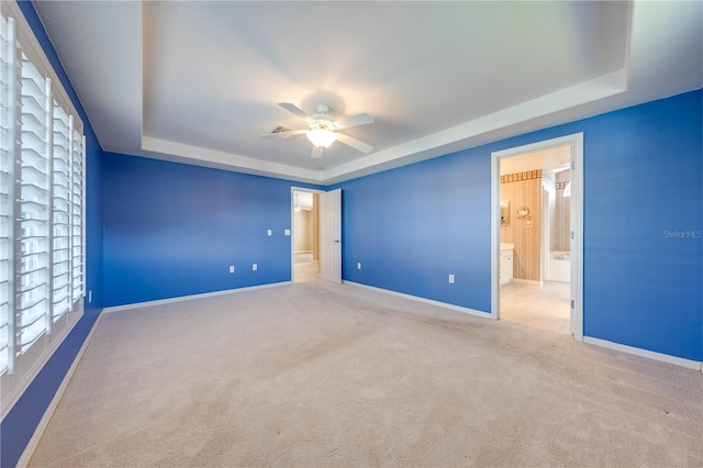 empty room featuring ceiling fan, a tray ceiling, and light carpet