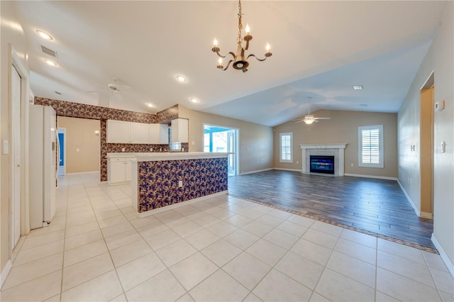 unfurnished living room with vaulted ceiling, plenty of natural light, ceiling fan with notable chandelier, and light tile patterned floors