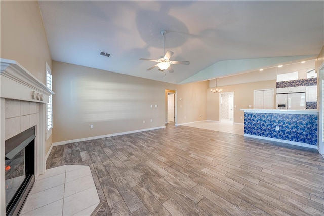 unfurnished living room with a tile fireplace, lofted ceiling, ceiling fan with notable chandelier, and light wood-type flooring