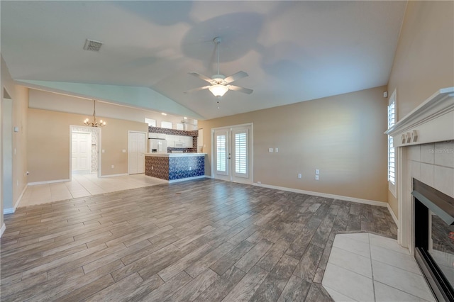 unfurnished living room with a tiled fireplace, lofted ceiling, ceiling fan with notable chandelier, and french doors