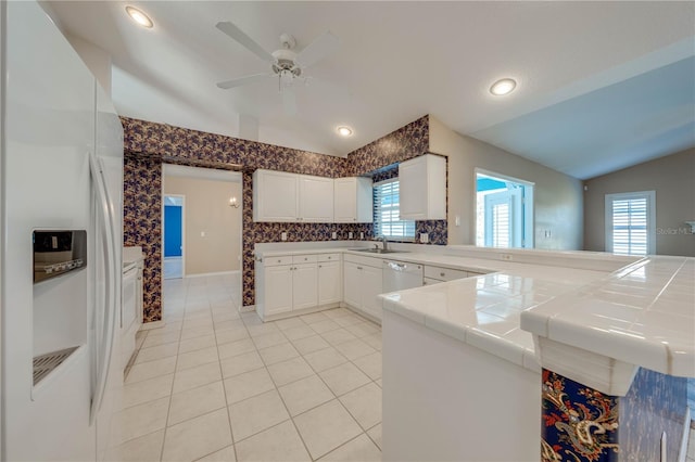 kitchen with vaulted ceiling, white cabinetry, white refrigerator with ice dispenser, tile countertops, and kitchen peninsula