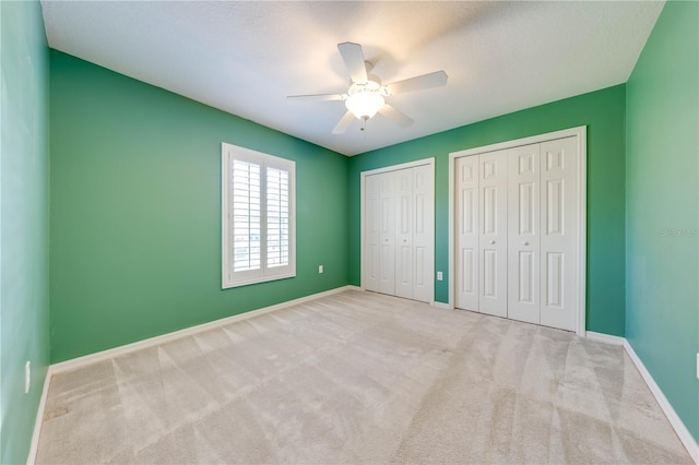 unfurnished bedroom featuring multiple closets, ceiling fan, and light carpet