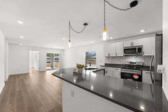 kitchen featuring white cabinetry, sink, hanging light fixtures, light hardwood / wood-style floors, and stainless steel appliances