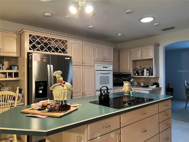 kitchen featuring black appliances, light tile patterned floors, a kitchen island, ceiling fan, and cream cabinetry