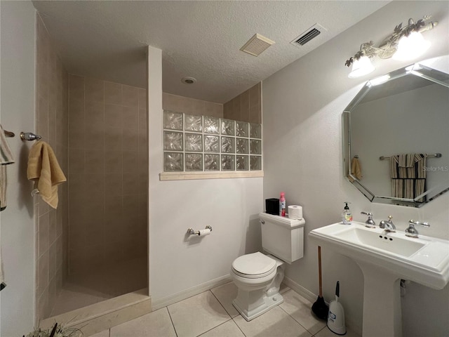 bathroom with tile patterned flooring, tiled shower, a textured ceiling, and toilet