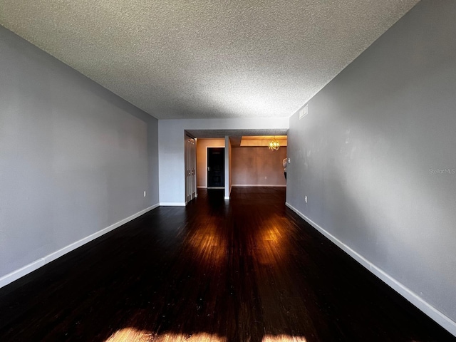 spare room with dark wood-type flooring, a textured ceiling, and a notable chandelier