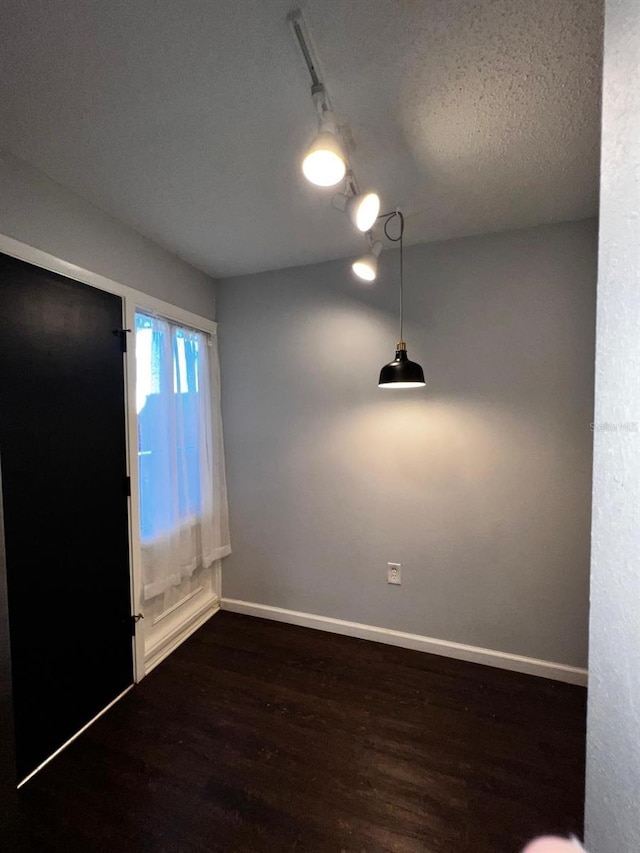 unfurnished room featuring track lighting and dark hardwood / wood-style floors