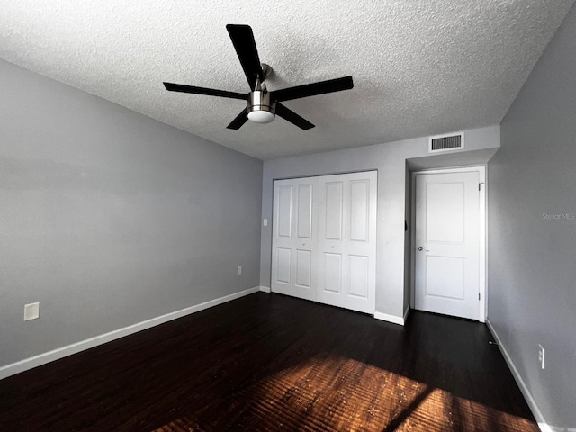 unfurnished bedroom featuring dark hardwood / wood-style floors, a textured ceiling, ceiling fan, and a closet