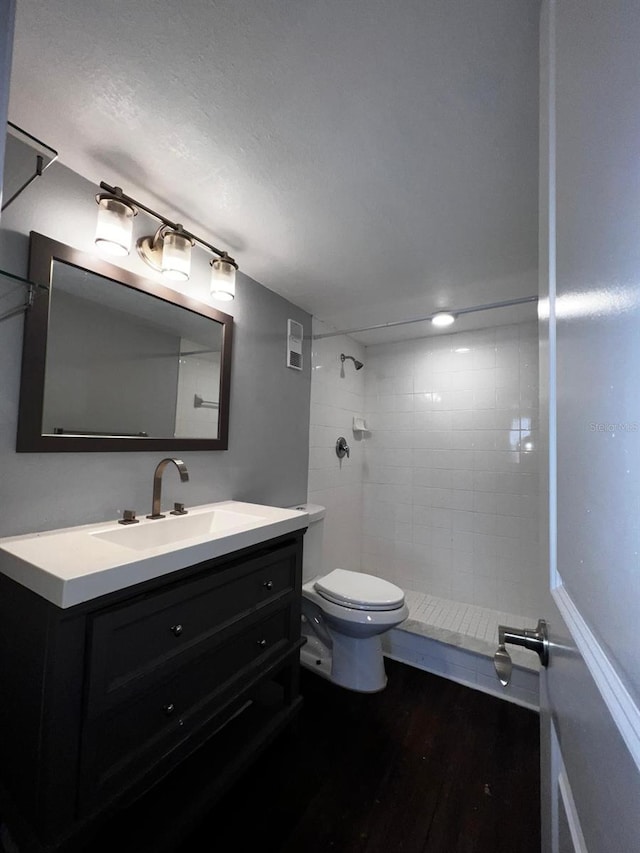 bathroom with vanity, wood-type flooring, a tile shower, and toilet