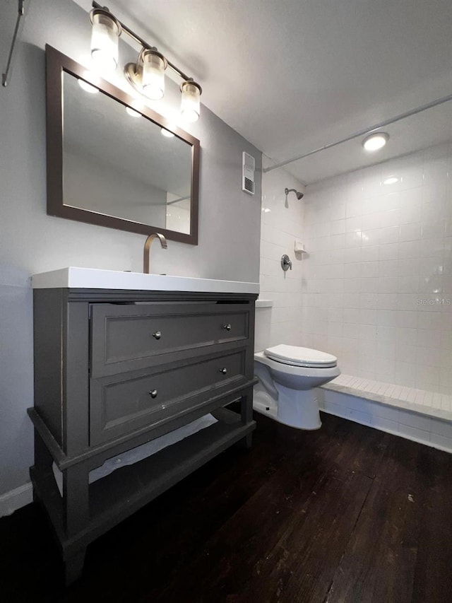 bathroom featuring vanity, hardwood / wood-style flooring, toilet, and tiled shower