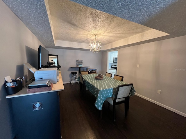 dining space featuring dark wood-type flooring, a tray ceiling, an inviting chandelier, and a textured ceiling