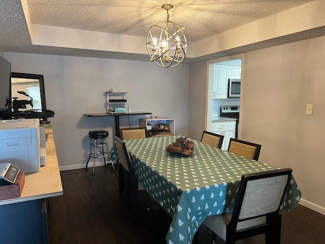 dining space featuring dark wood-type flooring, a chandelier, a textured ceiling, and a tray ceiling