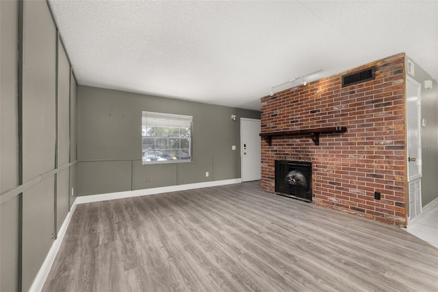 unfurnished living room with track lighting, a textured ceiling, a fireplace, and light hardwood / wood-style floors