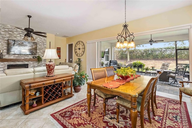 dining space featuring a stone fireplace, ceiling fan with notable chandelier, and light tile patterned floors