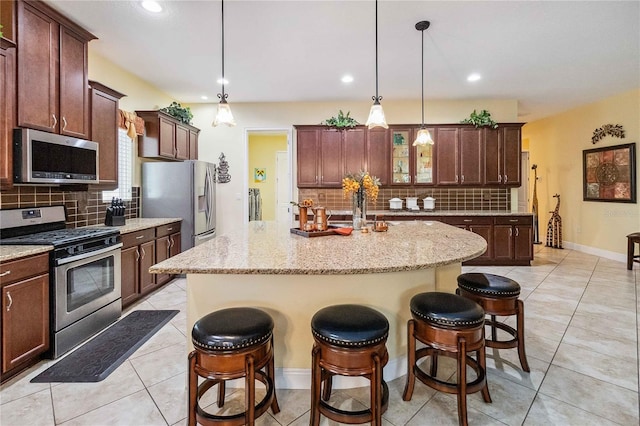 kitchen with pendant lighting, backsplash, stainless steel appliances, and a center island with sink