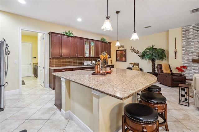 kitchen with stainless steel refrigerator, decorative light fixtures, sink, a breakfast bar area, and light tile patterned floors